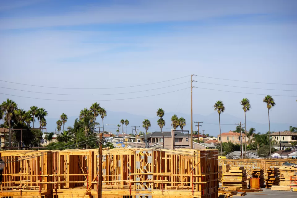 Wood-frame apartment building under construction with tall palm trees and power lines in background.